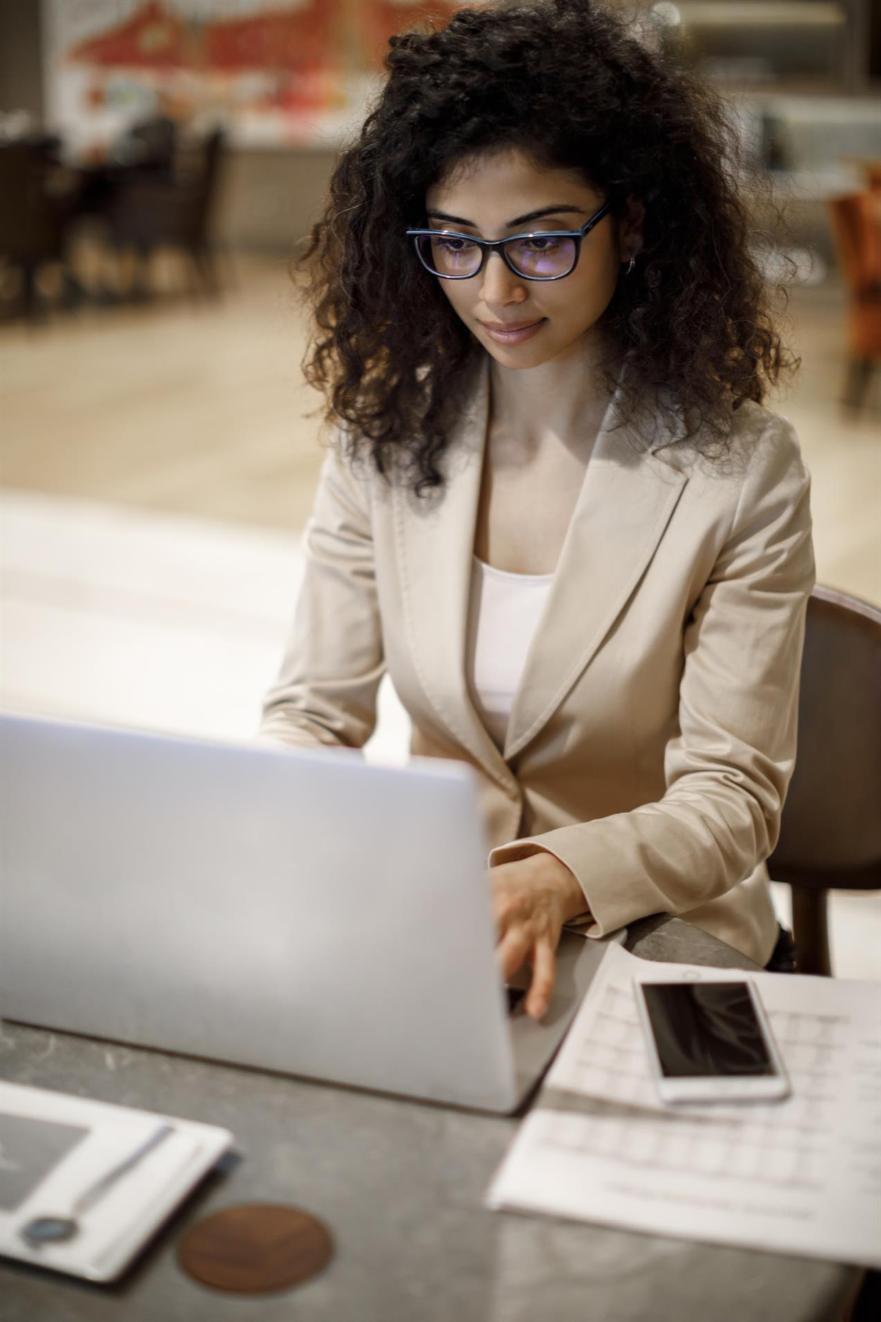A woman with black curly hair, A woman sitting around the table on laptop.