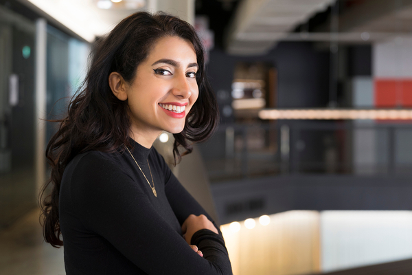 En person står selvsikkert og smiler til kameraet i et arbejdsmiljø.