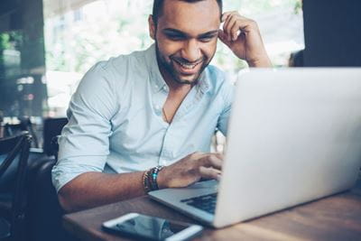 An employee sitting at a table, smiling while using a computer, conveying a positive attitude in a work setting.