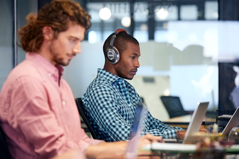 Twee medewerkers aan een tafel, geconcentreerd op hun computerscherm in een moderne kantooromgeving.